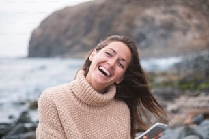 Portrait of happy young woman using the mobile phone. Sea and mountain on the background.