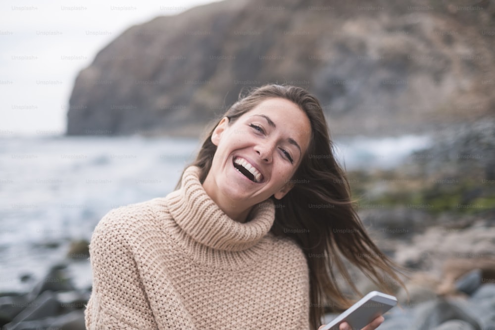 Portrait of happy young woman using the mobile phone. Sea and mountain on the background.