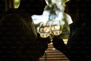 白ワインのグラスを持ち、感嘆の眼差しで見つめ合う、見分けがつかないロマンチックなカップルのシルエット