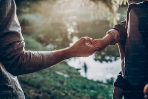 father and little son holding hands in sunlight. father's hand lead his child son in summer forest nature outdoor, trust, protecting, care, parenting family concept. road to life.