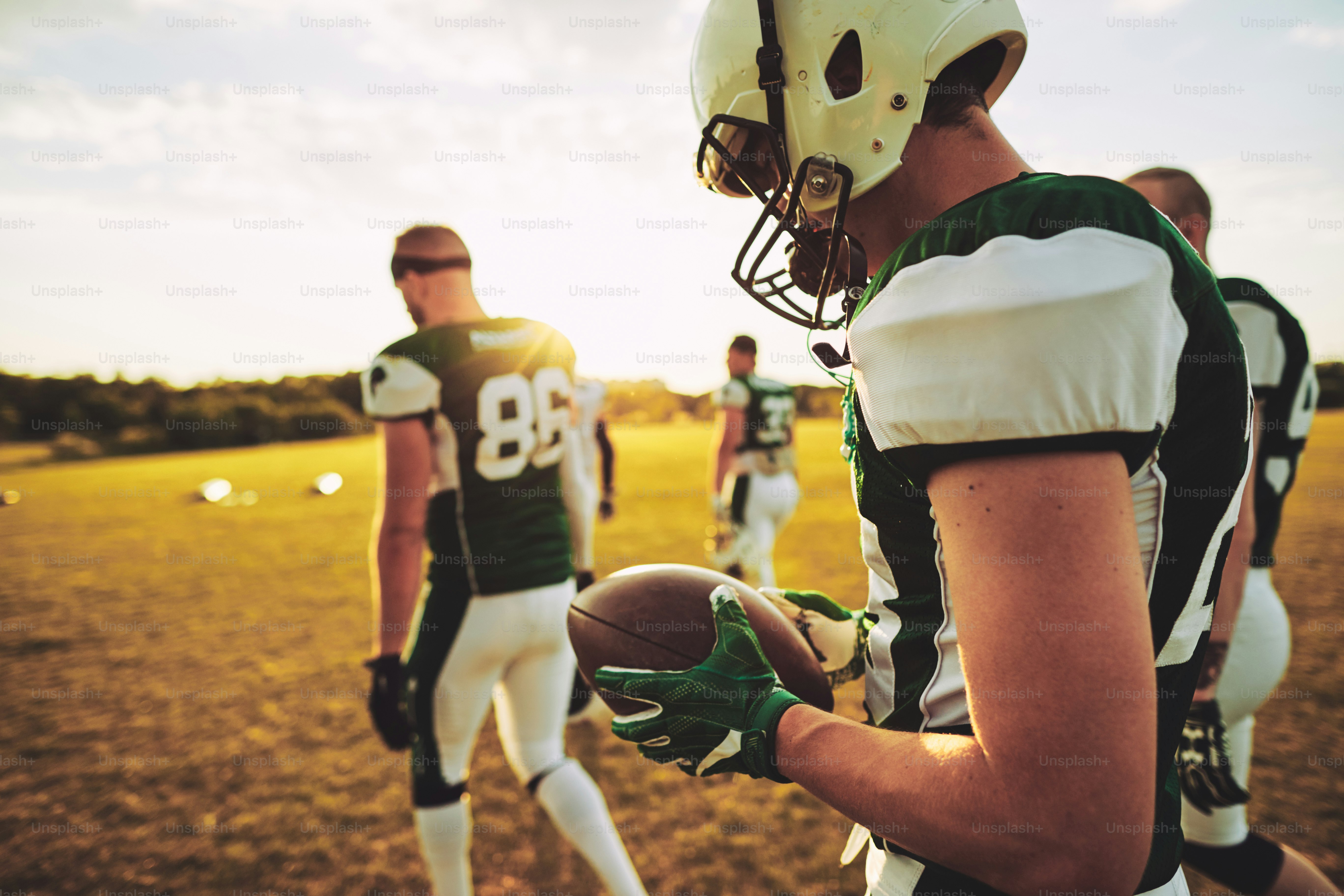 American Football Quarterback und seine Teamkollegen gehen nach einem Training an einem sonnigen Nachmittag gemeinsam vom Feld