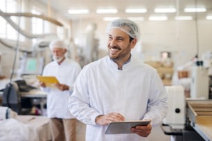 Uomo sorridente che usa la compressa mentre si trova in una fabbrica di alimenti.