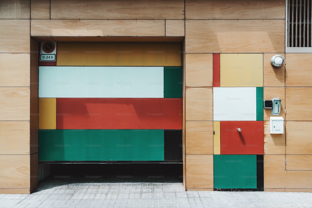 Multicolored fancy wooden facade of an ordinary house on a street of Barcelona: partly opened garage door, smaller entrance door with intercom and mailbox near