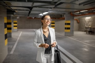 Joven mujer de negocios caminando con las llaves del coche en el aparcamiento subterráneo del nuevo edificio residencial