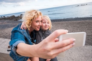 cheerful mother and son blondes both stay together outdoor in leisure activity taking selfie pictures with smart phone technology ready to share it on social networks for friends away