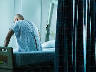 Un homme en blouse d’hôpital assis sur un lit d’hôpital