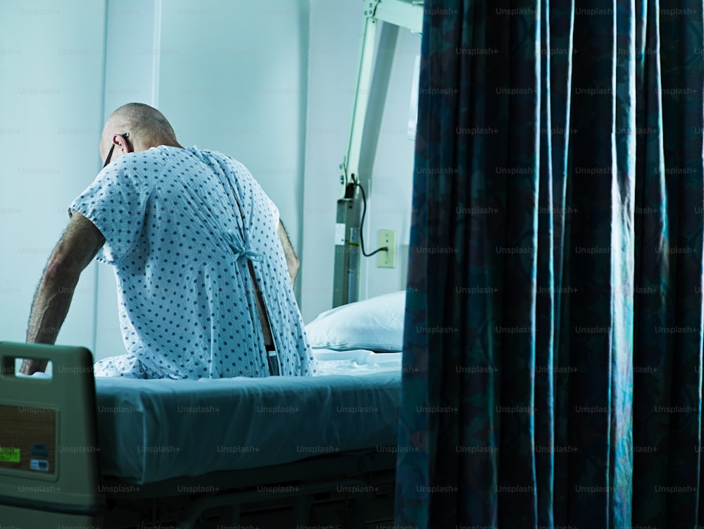 Un hombre con bata de hospital sentado en una cama de hospital