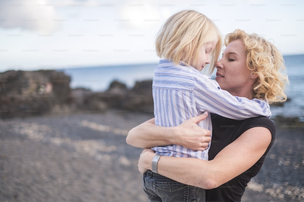 young beautiful blonde east Europe mother woman kiss her son while hug him with love and togetherness emotion and feeling. enjoy life and lifestyle for nice family outdoor - single mom