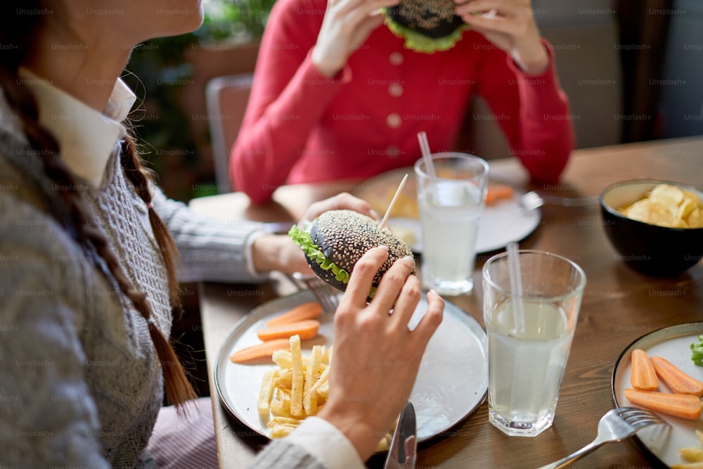 Adolescente y su amiga almorzando hamburguesas con queso y papas fritas en un café de comida rápida