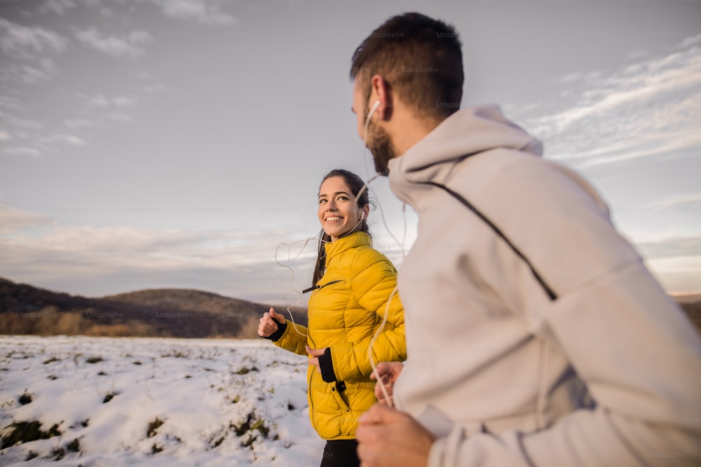 Side view of a young fitness couple running in nature in winter.