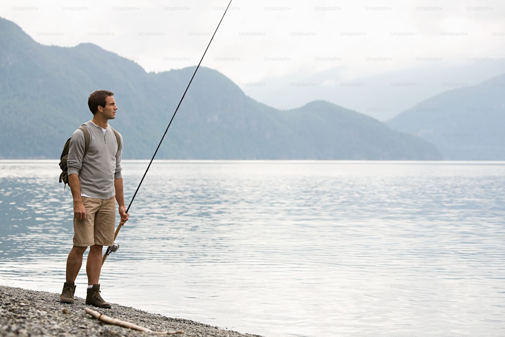 a man standing on the shore of a lake while holding a fishing pole