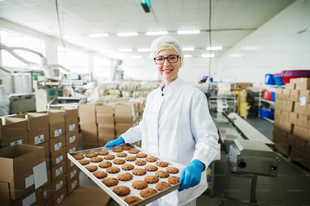 Female worker standing and holding plate with cookies. Food factory interior.