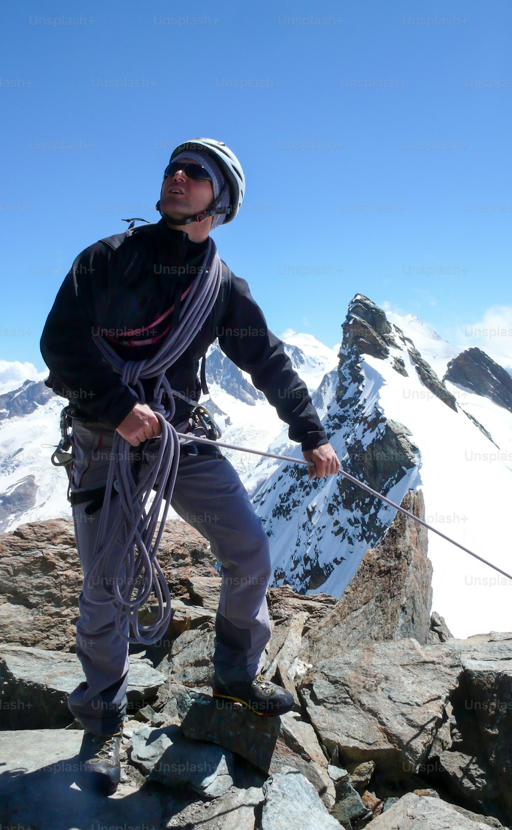 guía de montaña de pie en el pico de una montaña rocosa y tirando de un cliente en una cuerda con un fantástico paisaje montañoso de los Alpes suizos sobre Zermatt detrás de él