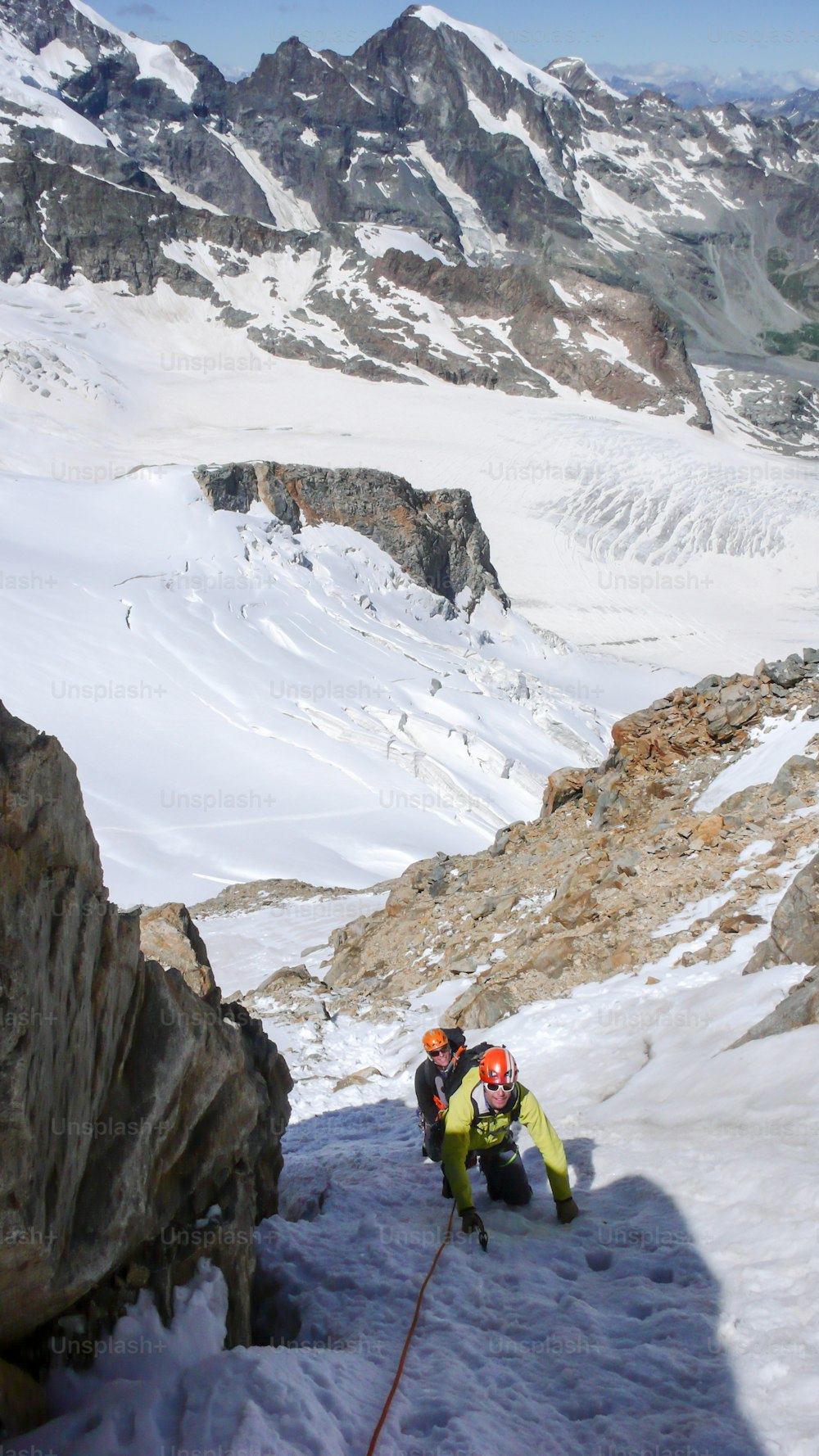 A mountain guide leading male client to the summit of a high alpine peak on a beautiful summer day