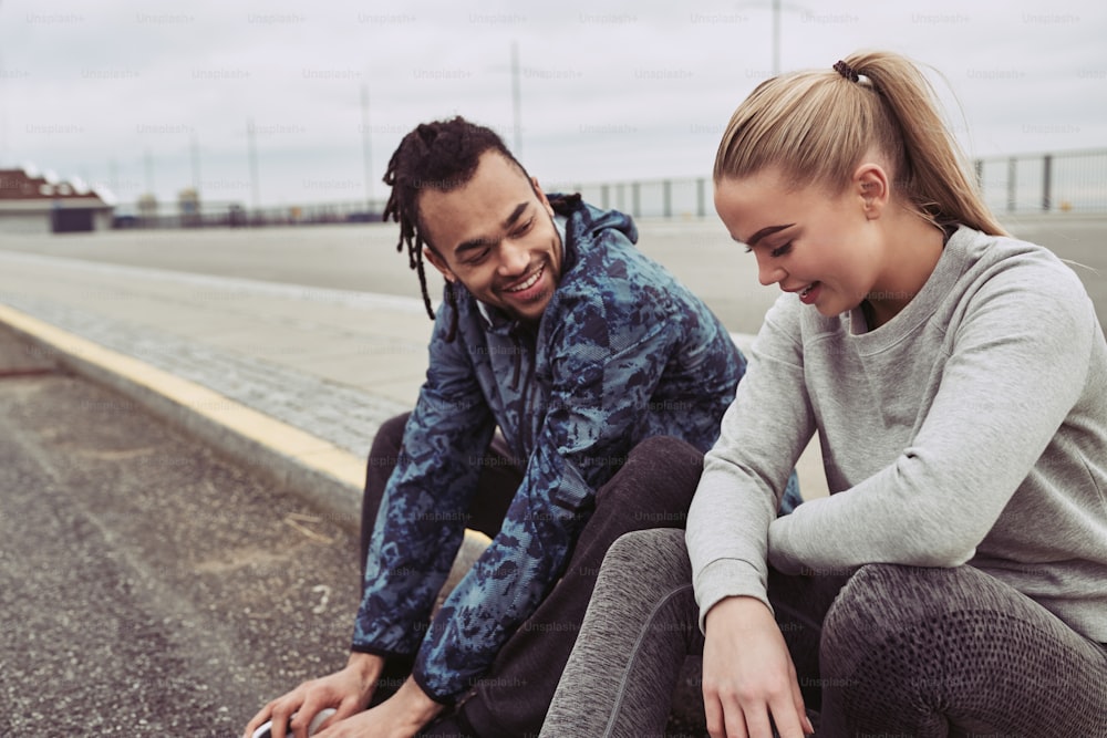 Smiling young couple taking a break on the side of a road after runnng together on an overcast day