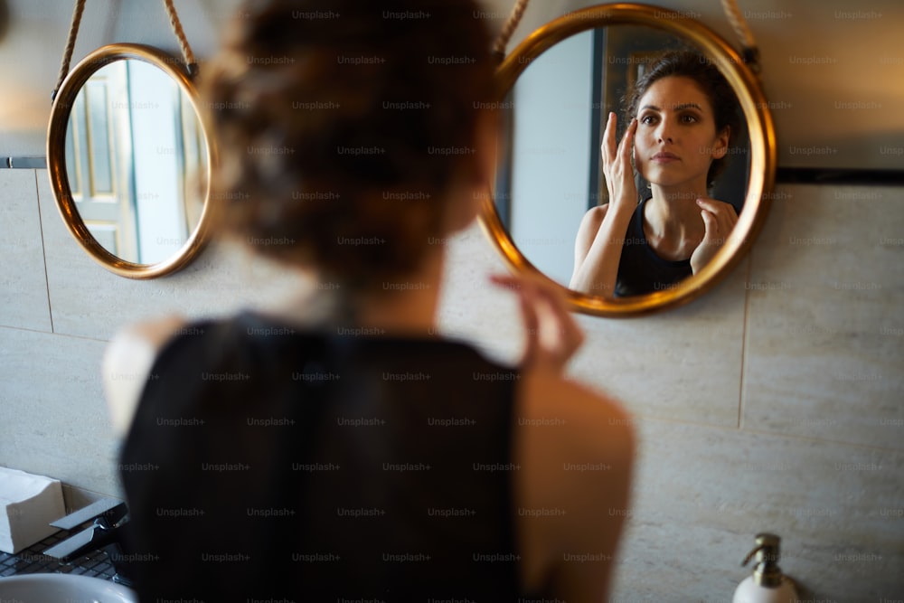 Bonita mujer joven que se mira en el espejo y refresca su maquillaje en el lavabo