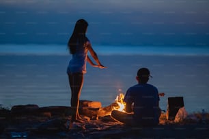 焚き火のそばの海岸で休むカップル。夕方の夜の時間帯