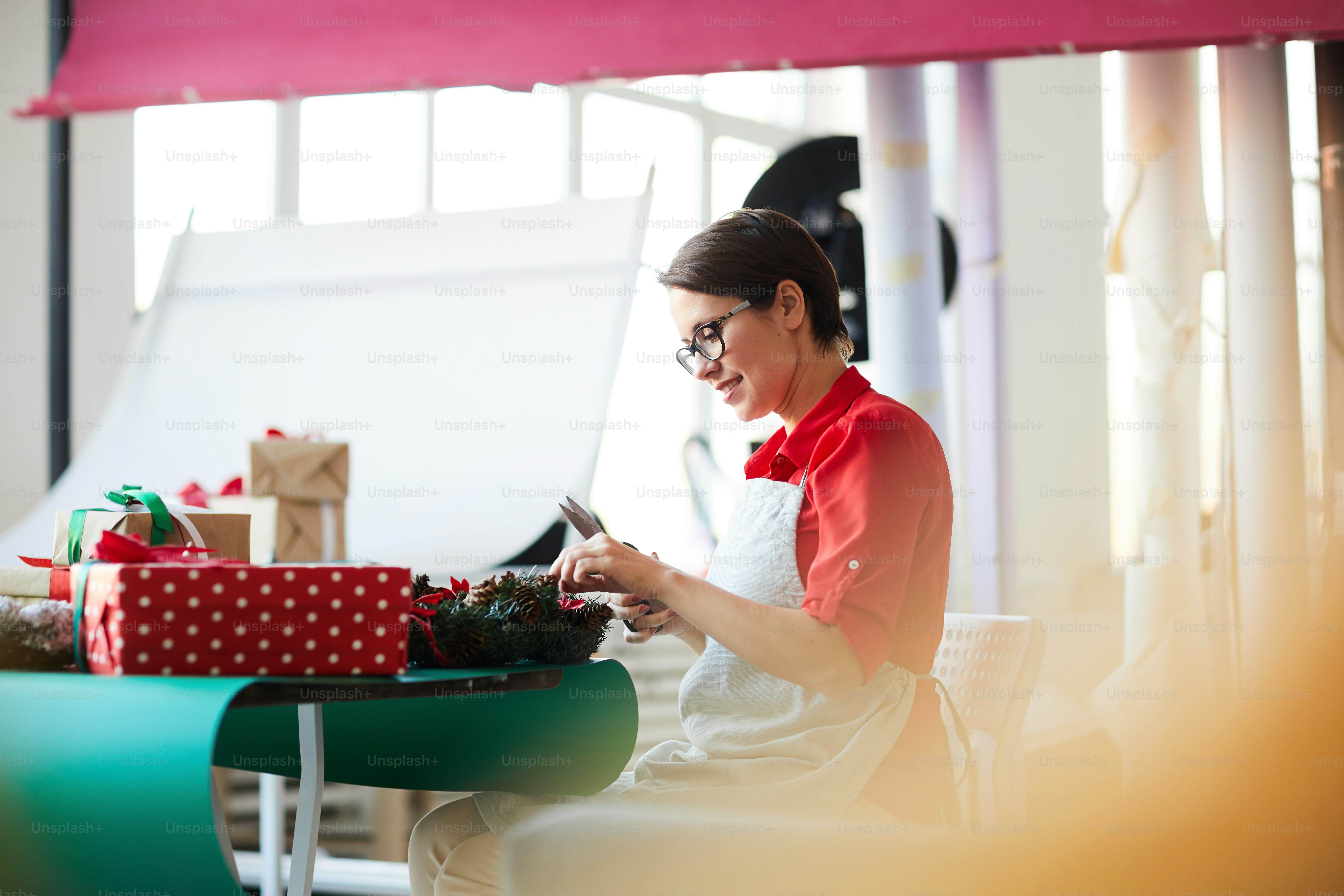Young designer in workwear sitting by table and preparing xmas staff for holiday