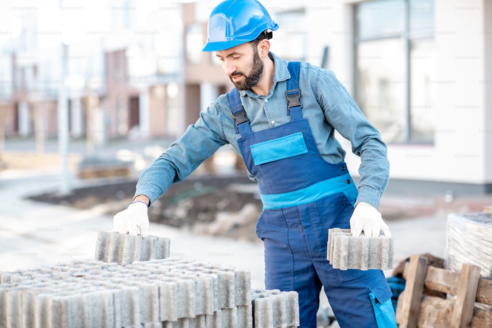 Builder in uniform taking paving blocks from the pallet working on the construction site outdoors