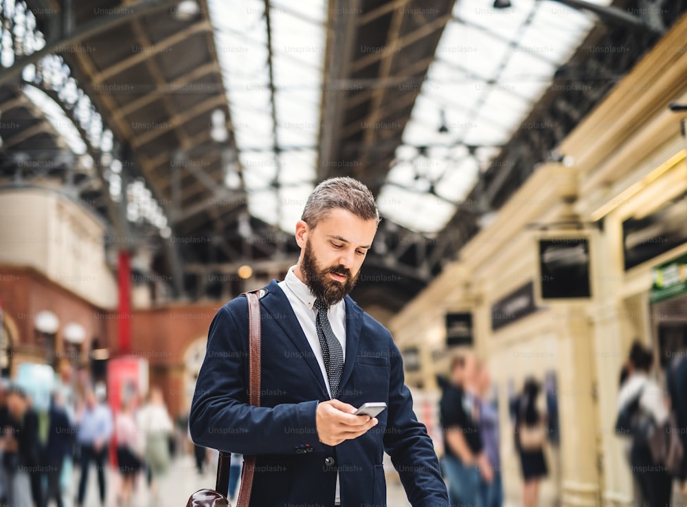 Homme d’affaires heureux avec un smartphone à la gare de Trian à Londres, en train d’envoyer des SMS.