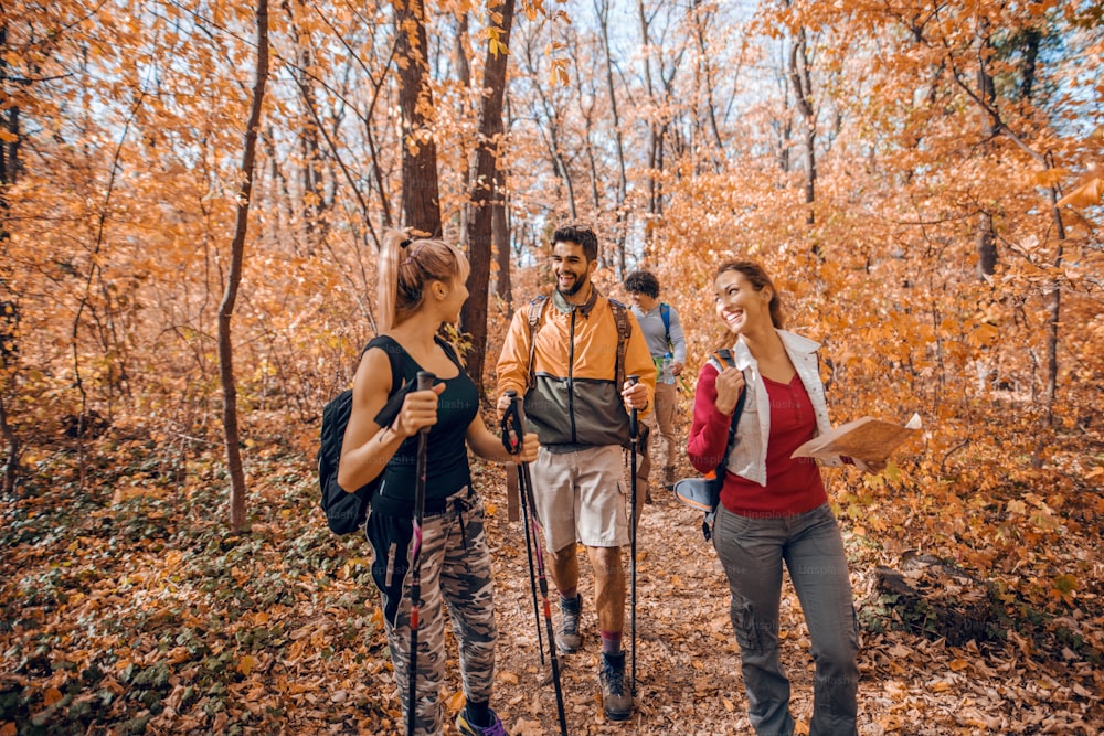 Pequeno grupo feliz de caminhantes que caminham na floresta no outono. Mulher segurando o mapa enquanto outros a seguem. Conceito de aventura.
