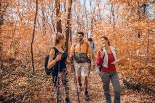 가을에 숲속을 걷는 작은 행복한 등산객 그룹. 다른 사람들이 그녀를 따라가는 동안 지도를 들고 있는 여자. 모험 개념입니다.