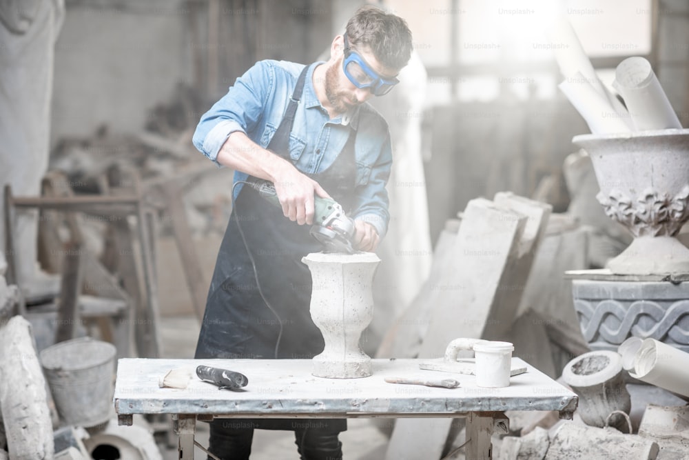 Bildhauer in Arbeitsware schleifende Steinvase am Arbeitsplatz im alten stimmungsvollen Atelier