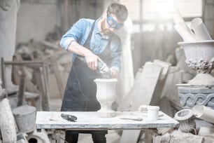 Sculptor in workware grinding stone vase at the working space in the old atmospheric studio