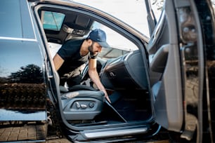 Professional cleaner in black t-shirt and cap vacuuming mats of a luxury car
