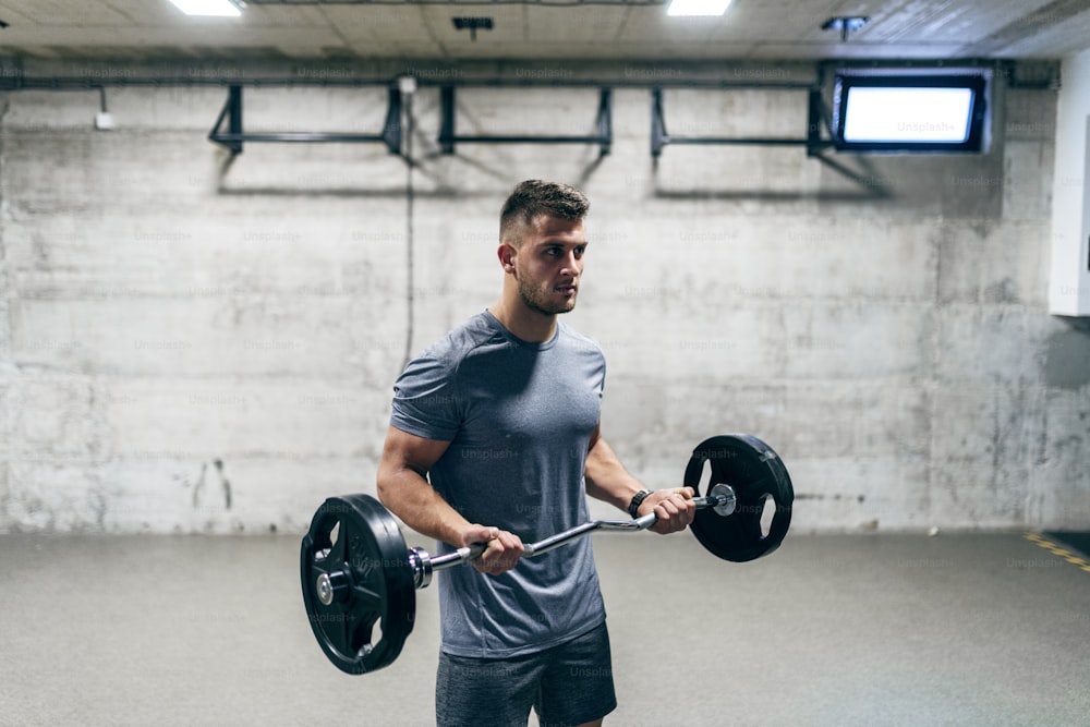 Focused young Caucasian man in sportswear lifting barbells. Wake up with determination, go to bed with satisfaction.