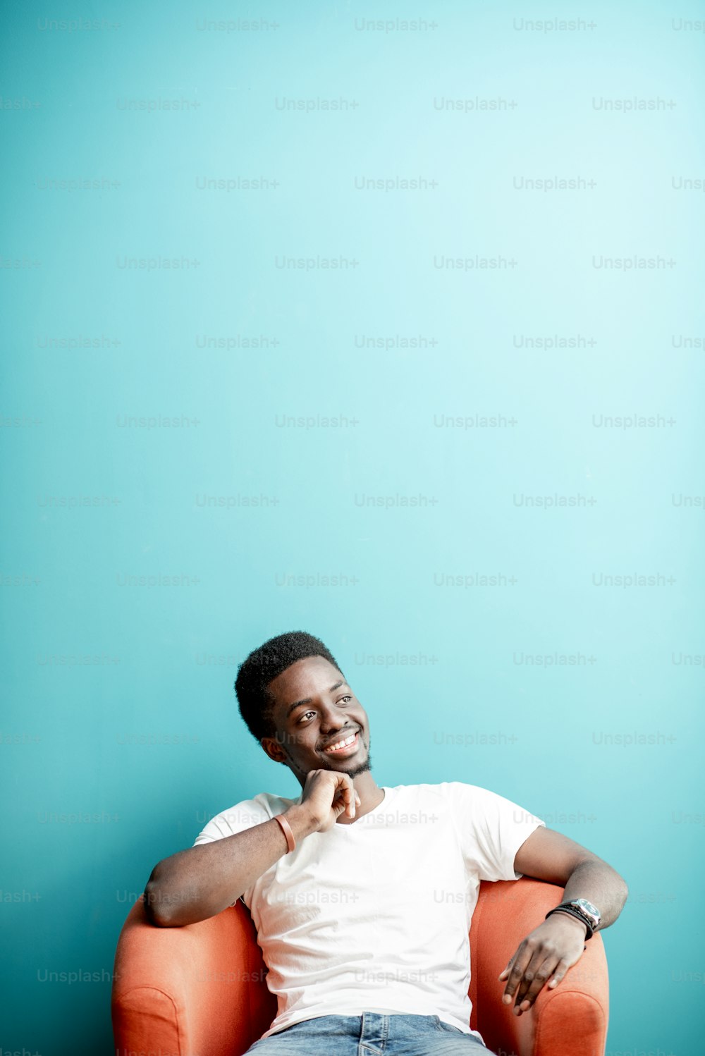Portrait of a young african man dressed in white t-shirt and jeans sitting on the chair on the colorful background. Image with copy space