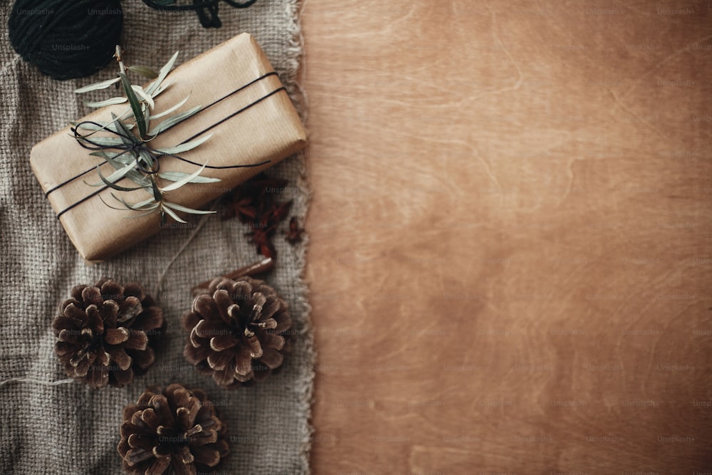 녹색 가지와 전나무 가지, 아니스, 솔방울, 소박한 나무 배경에 계피가 있는 세련되고 소박한 선물 상자. 간단한 에코 선물. 텍스트를 위한 공간입니다. 메리 크리스마스 컨셉, 분위기 있는 플랫 레이