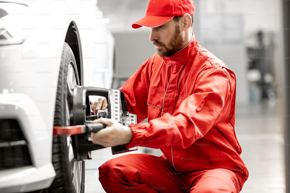 Handsome auto mechanic in red uniform fixing disk for wheel alignment at the car service