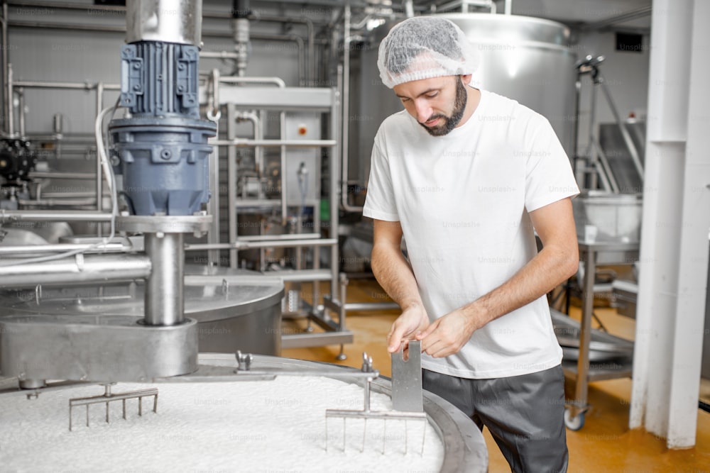 Homem misturando leite no tanque inoxidável durante o processo de fermentação na fabricação de queijo
