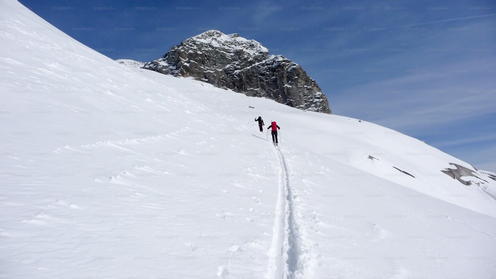 푸른 하늘 아래 겨울에 오스트리아 알프스의 먼 산봉우리로 하이킹하는 두 명의 오지 스키 선수