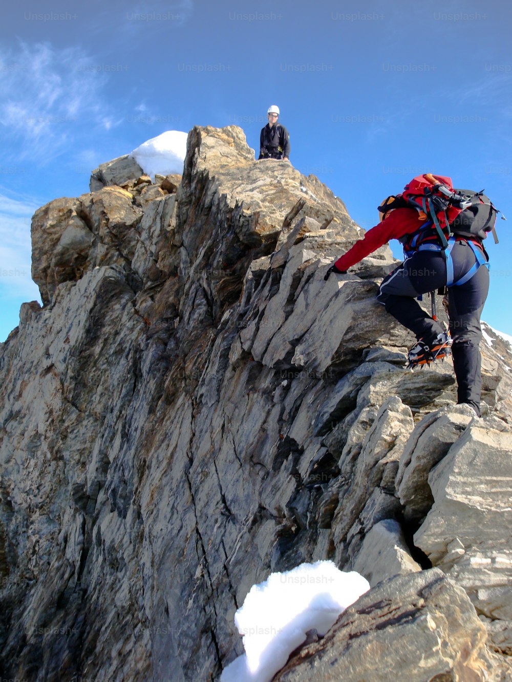 Bergsteigerin und Bergsteigerin auf dem Weg zu einem Hochgebirgsgipfel entlang eines schmalen Felsrückens in den Schweizer Alpen