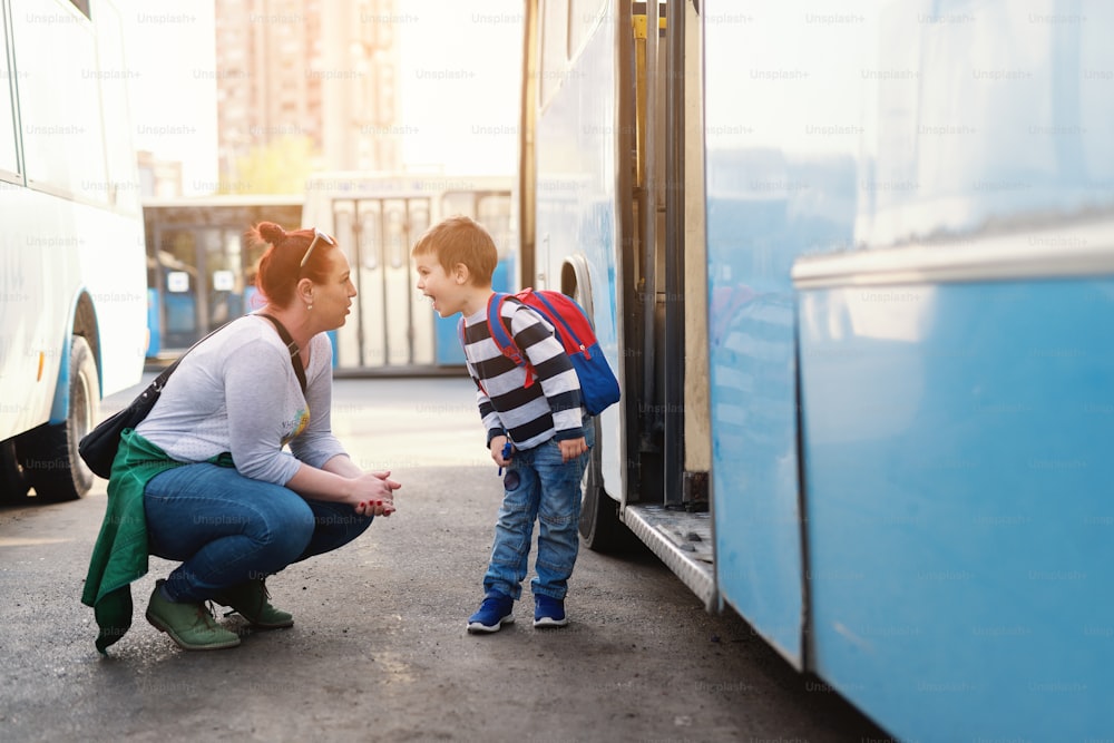 バスの前にしゃがみ込みながら息子と話す母親。学校に行く子供。