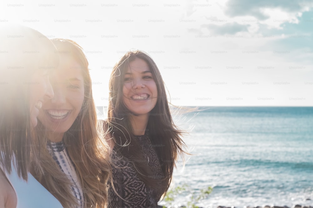 3 giovani donne camminano sulla spiaggia guardandosi, ridendo e trascorrendo del tempo libero insieme. in una bella giornata d'estate. con il sole e il mare come sfondo. Colori blu e retroilluminazione bianca brillante