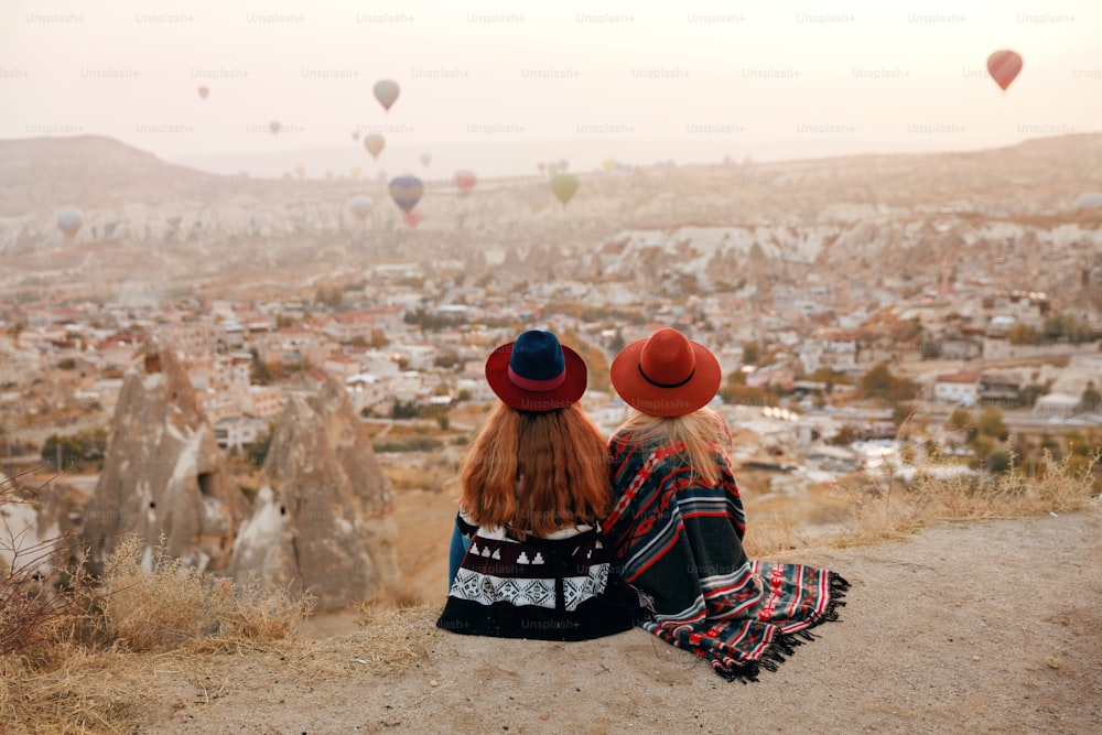 Menschen reisen. Frauen mit Hüten sitzen auf einem Hügel und genießen das Fliegen von Heißluftballons auf Kappadokien Türkei. Hohe Auflösung