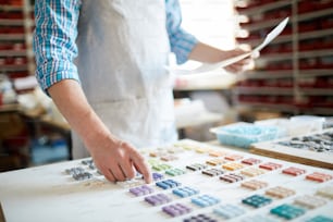 Mid section portrait of unrecognizable man pointing at samples while choosing colored square tiles for interior decoration, copy space