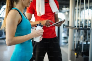 Fit young active woman with plastic bottle of water watching online video shown by her trainer or mate at break