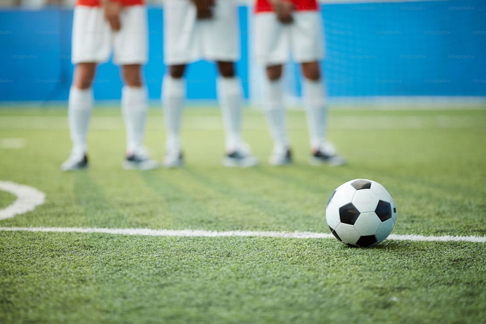 Soccer ball on green football field by dividing line and legs of three players on background