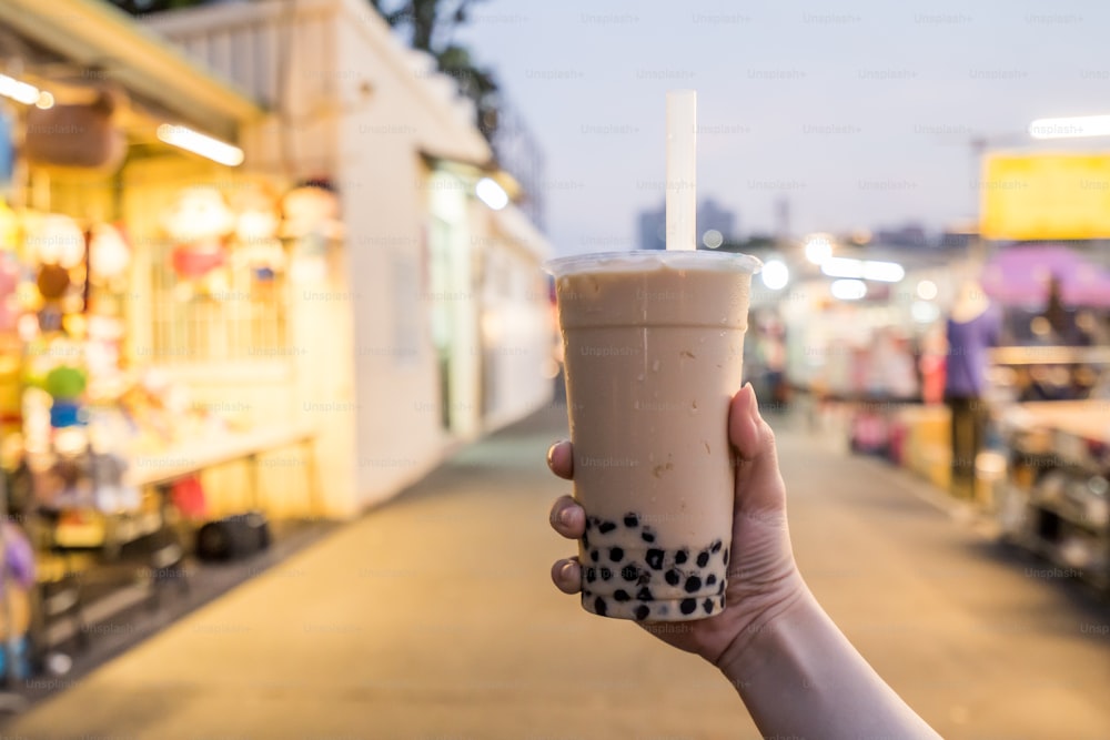 若い女性が台湾の夜市でストロー付きのタピオカミルクティーのプラスチックカップを持っている、台湾の珍味、クローズアップ。