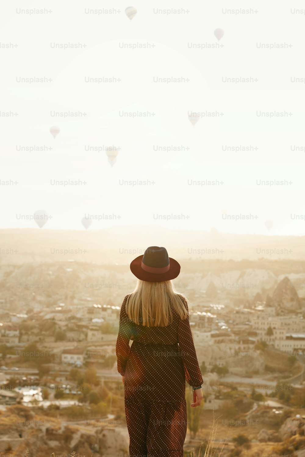 Travel. Beautiful Woman In Hat On Hill With Flying Hot Air Balloons In Sky. Female Traveling To Cappadocia. High Resolution