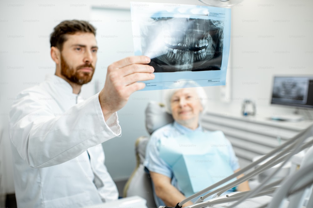 Donna anziana felice durante la consultazione con un bel dentista che mostra una radiografia panoramica nello studio dentistico