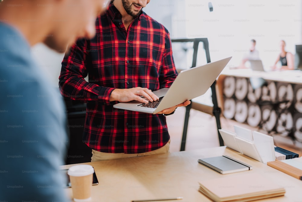 Positive handsome smiling man using his laptop while working with his colleague in the office