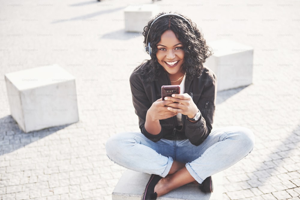 Portrait of a beautiful young pretty African American girl sitting on the beach or lake and listening to music in her headphones.