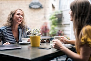Mujeres jóvenes con estilo que tienen una reunión amistosa con tazas de café mientras están sentadas en la mesa y charlan
