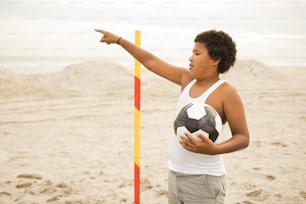 a woman pointing at a soccer ball on the beach