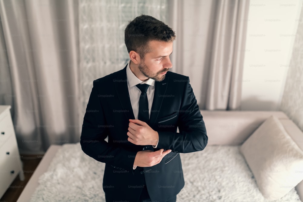 Portrait of young businessman tying cufflinks on jacket and looking away.
